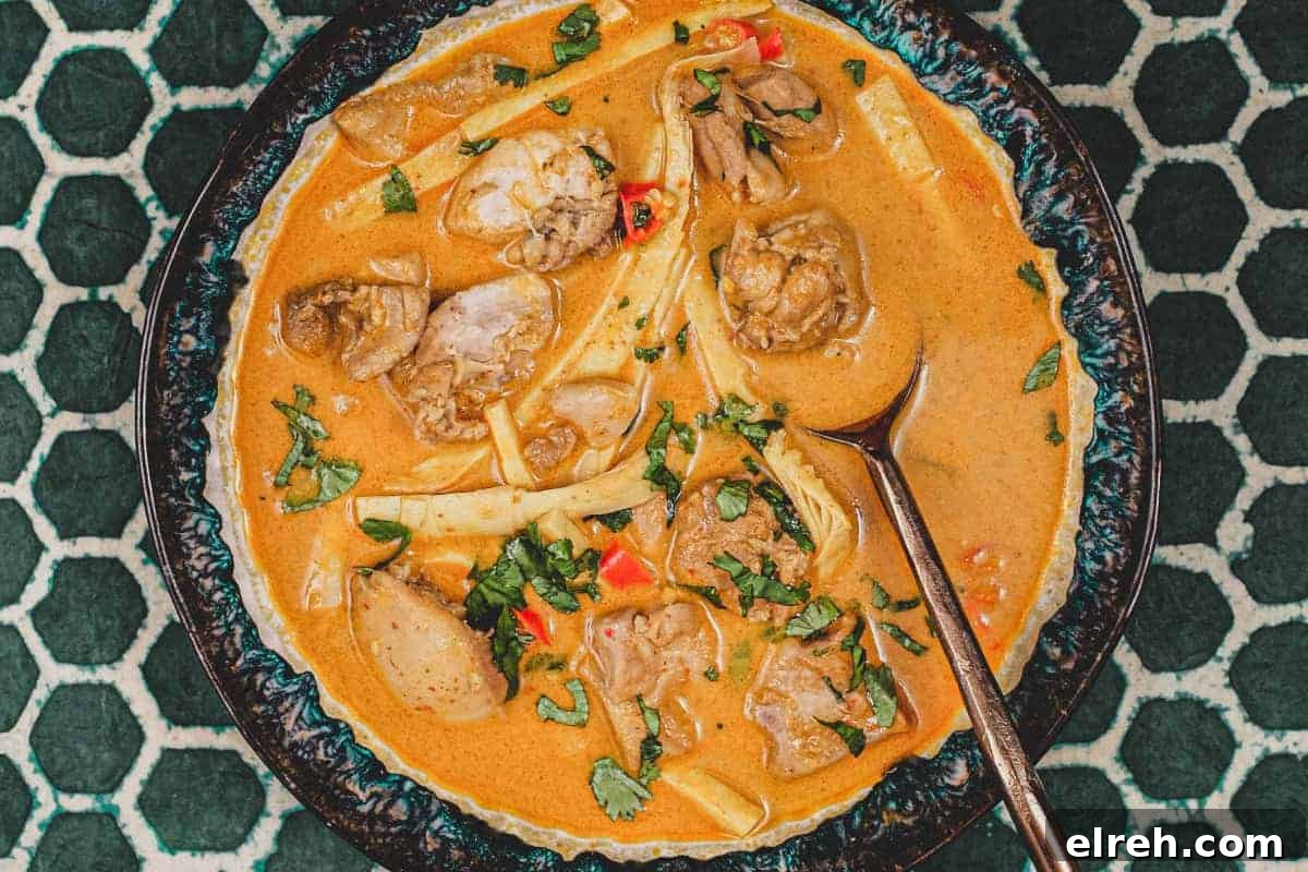A bowl of vibrant orange Laotian chicken curry and spoon on a green batik background 