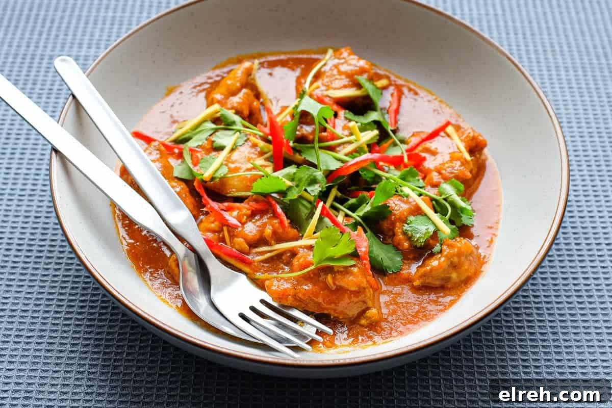 A bowl of Burmese chicken curry with fork and spoon