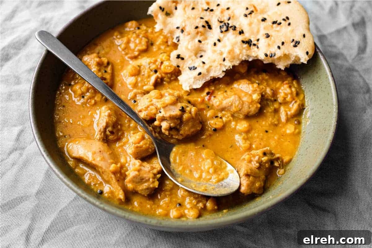 A bowl of lentil curry with a spoon and piece of naan bread