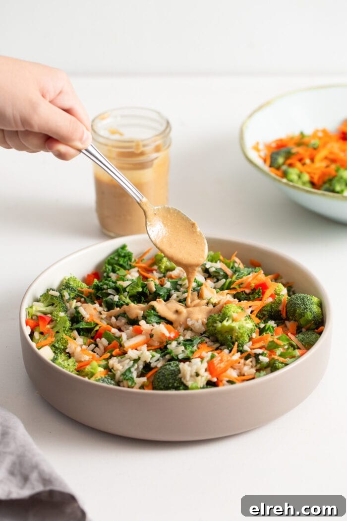 Hand adding a spoonful of peanut sauce to a kale salad.