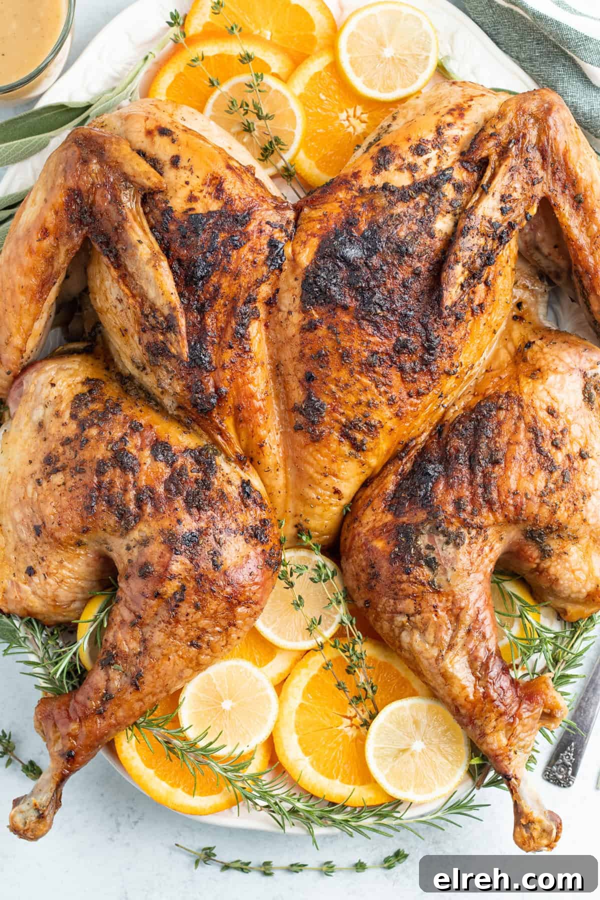 Overhead view of a grilled spatchcock turkey on a white serving platter garnished with lemon discs.