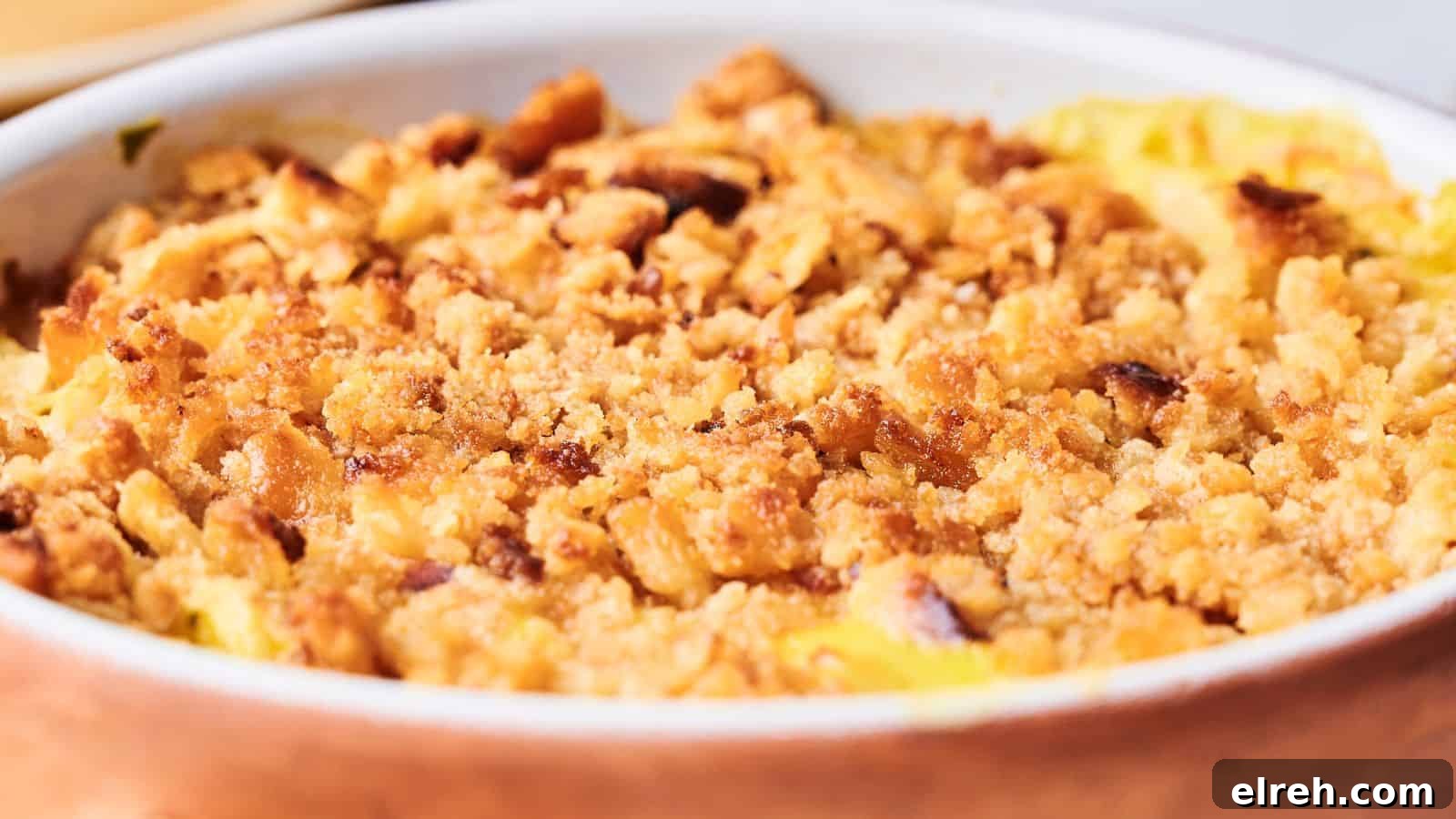 Close-up of a baked apple crumble dessert in a ceramic dish, featuring a golden-brown crumbly topping.