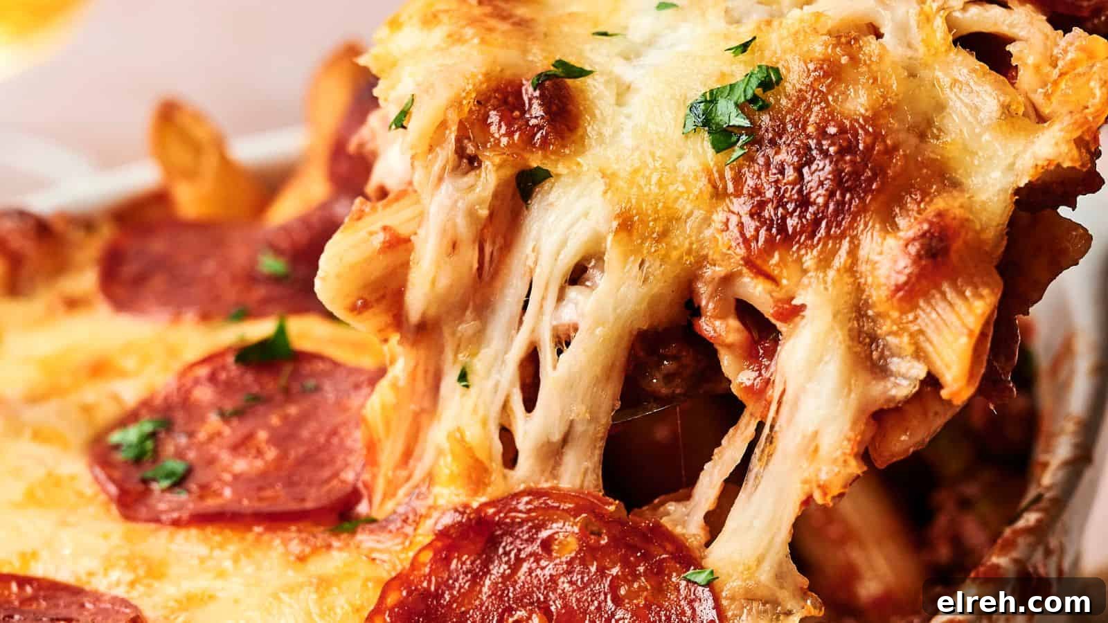 A close-up of a baked pasta dish with melted cheese, pepperoni slices, and herbs, showing a serving being lifted, revealing gooey cheese strands.