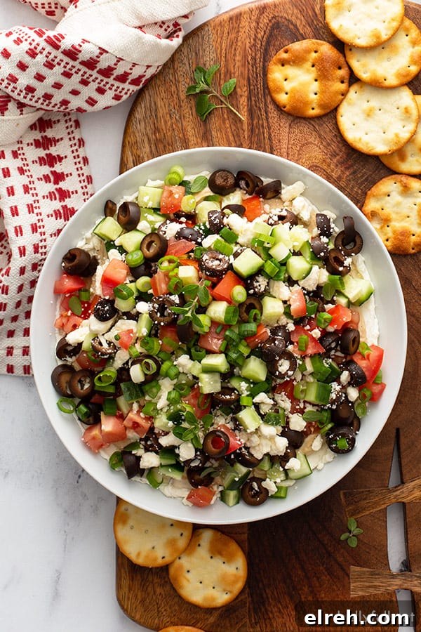 layered dip with cream cheese, hummus, olives, cucumber, and tomato