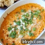Buffalo chicken dip in dish topped with blue cheese and green onion ready to serve.