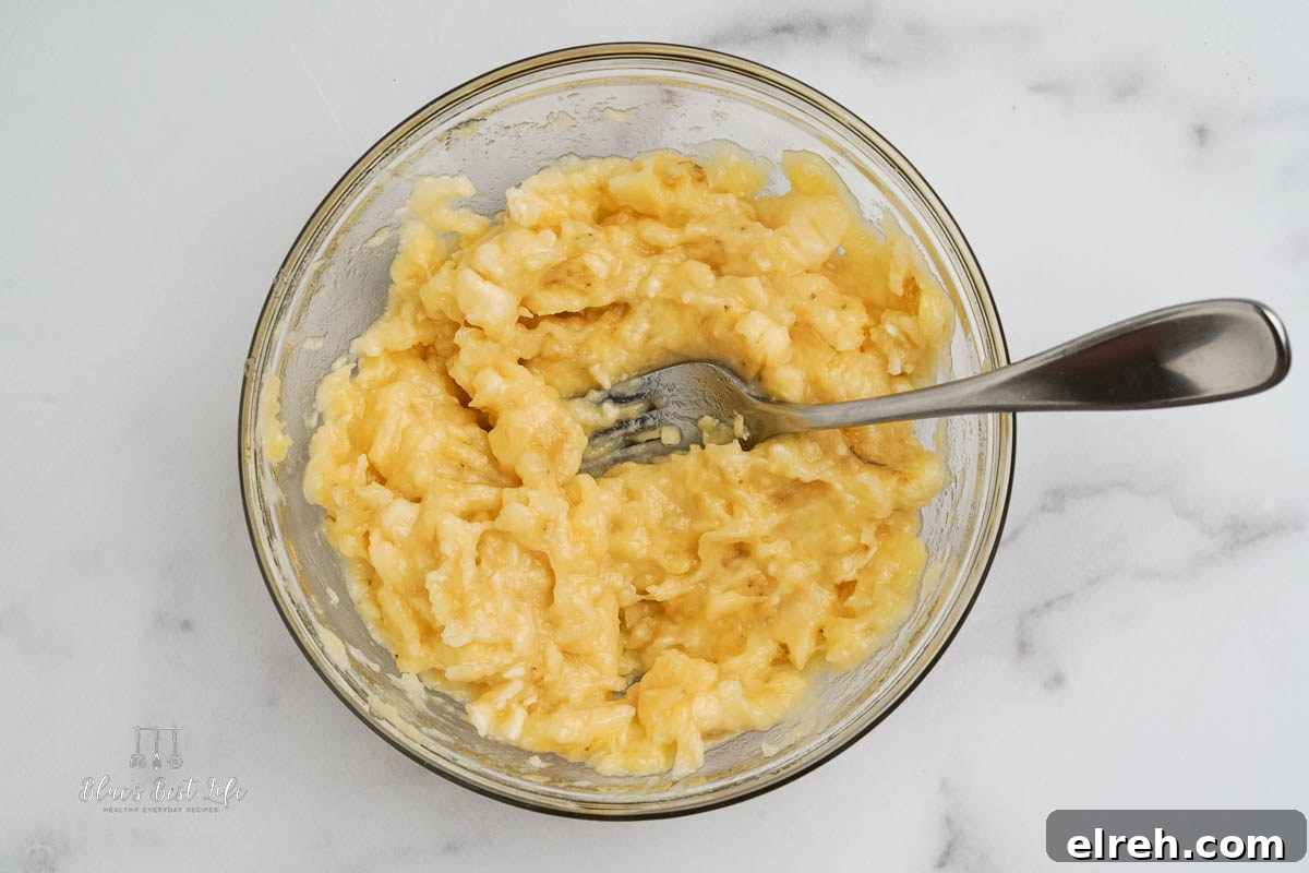 A clear bowl with bananas being mashed using a fork