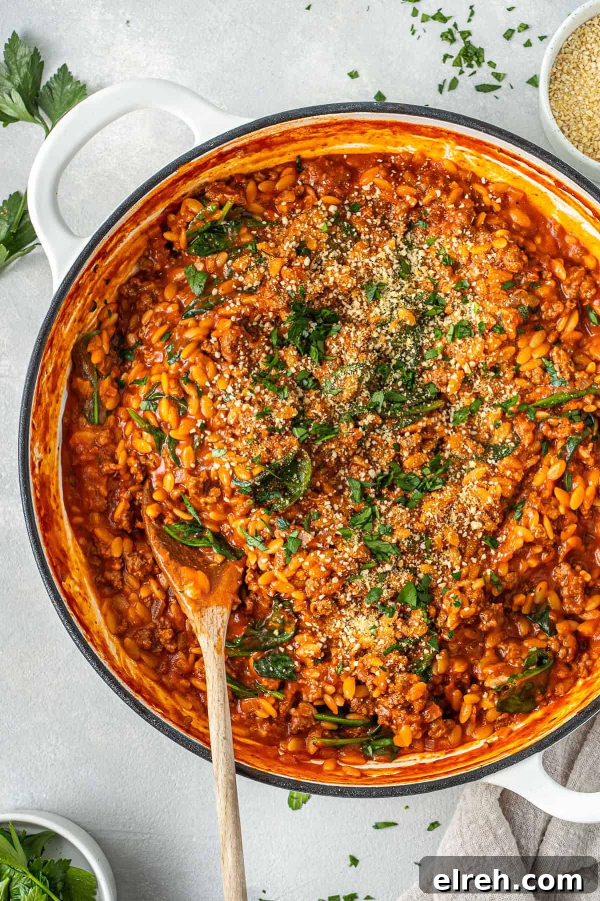 Creamy ground beef and orzo in a pot with a wooden spoon topped with dairy free parmesan and parsley.