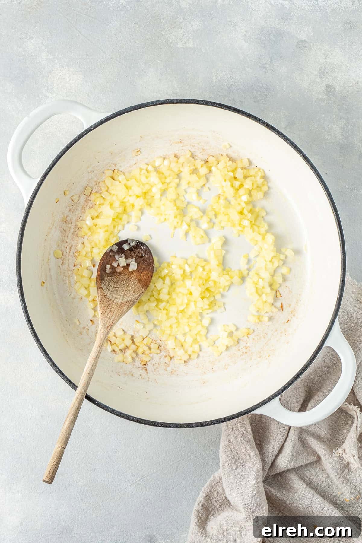 The onions frying in a pan with a wooden spoon.