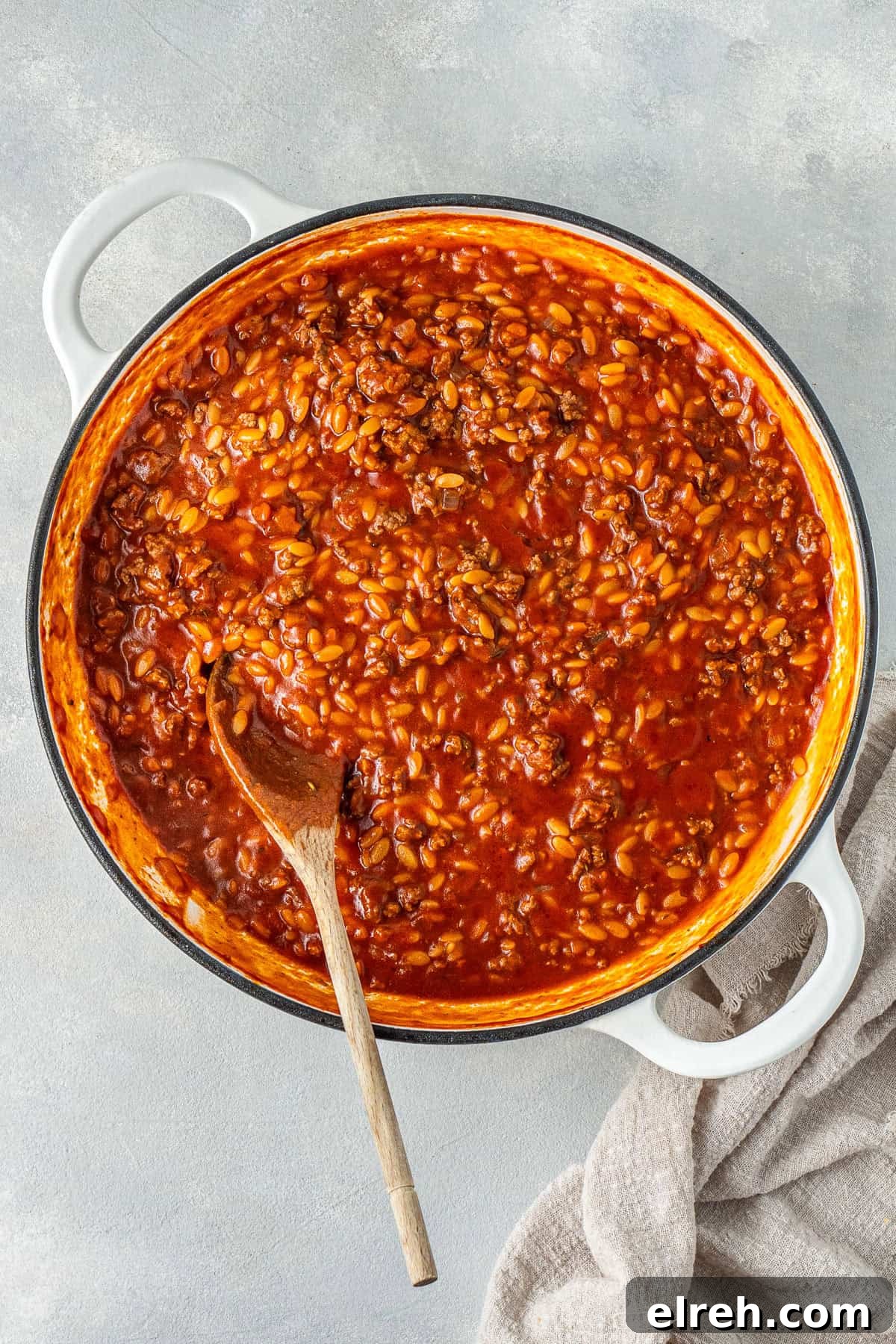 The cooked orzo in the sauce with a wooden spoon.