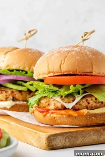 Two air fried turkey burgers with buns on a wood cutting board.