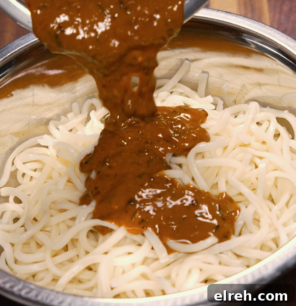 Spicy dan dan sauce being poured over cooked noodles in a metal bowl — ready to toss and serve.