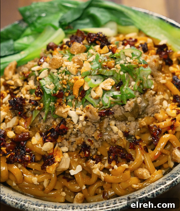 Full bowl of dan dan noodles garnished with scallions, peanuts, chili oil, and bok choy — spicy and savory Chinese noodle dish.