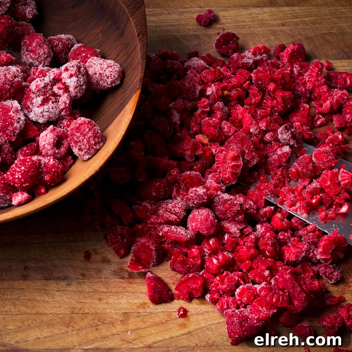 Raspberry Cupcakes Recipe with Cream Cheese Frosting 11 Chopping frozen raspberries into small pieces on a wood cutting board.