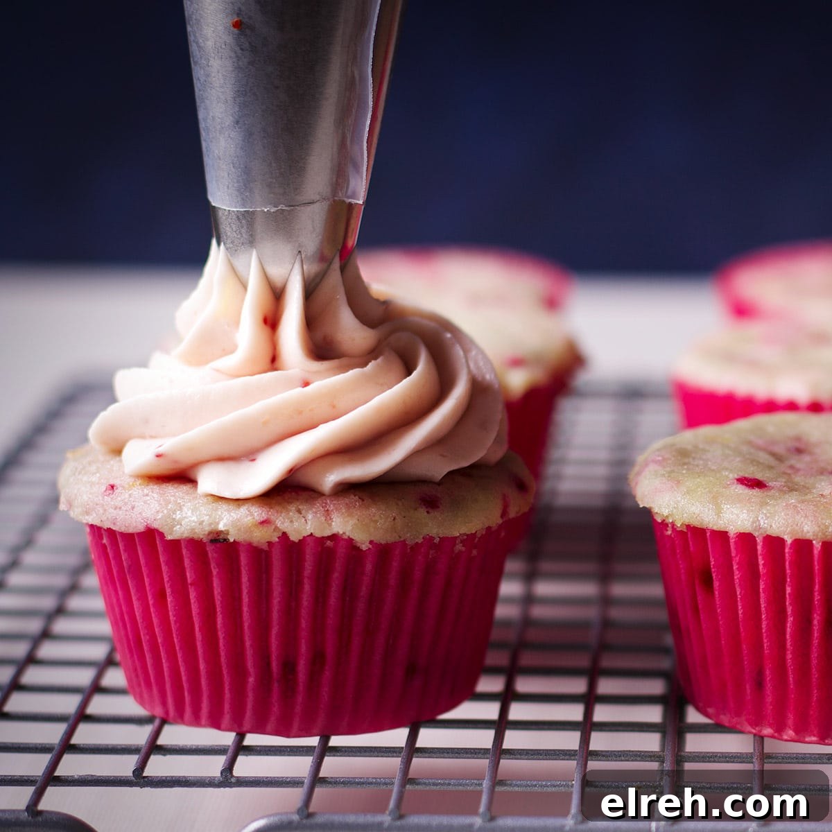 Raspberry Cupcakes Recipe with Cream Cheese Frosting 19 Using a pastry bag and cupcake tip to pipe a swirl of raspberry cream cheese frosting on a raspberry cupcake.
