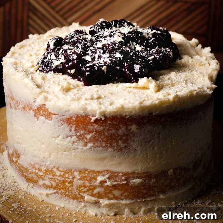 A white forest cake topped with white chocolate ganache buttercream and cherry sauce on a wood cake tray.