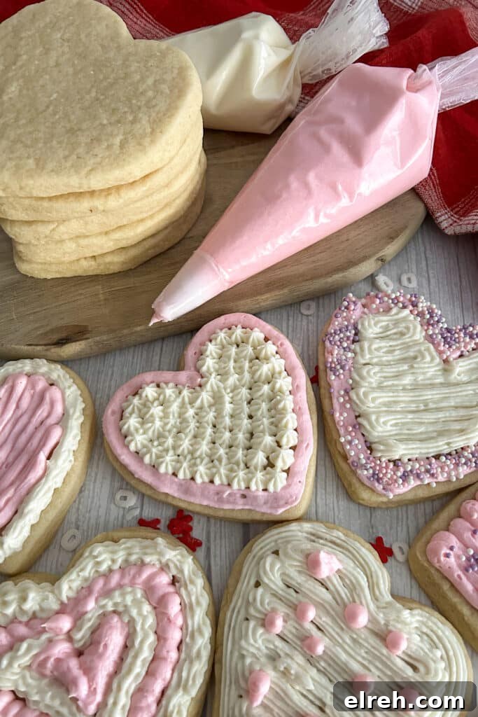 Valentines day cookies frosted and topped with sprinkles.  Piping bag with pink frosting and unfrosted cookies in the background