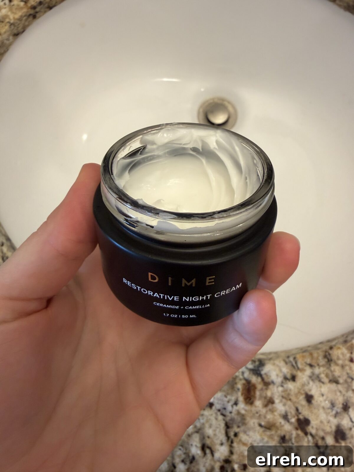 A hand holds an open jar of DIME Restorative Night Cream
