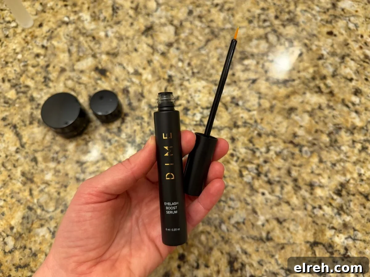 A hand holds an open tube of DIME Eyelash Boost Serum