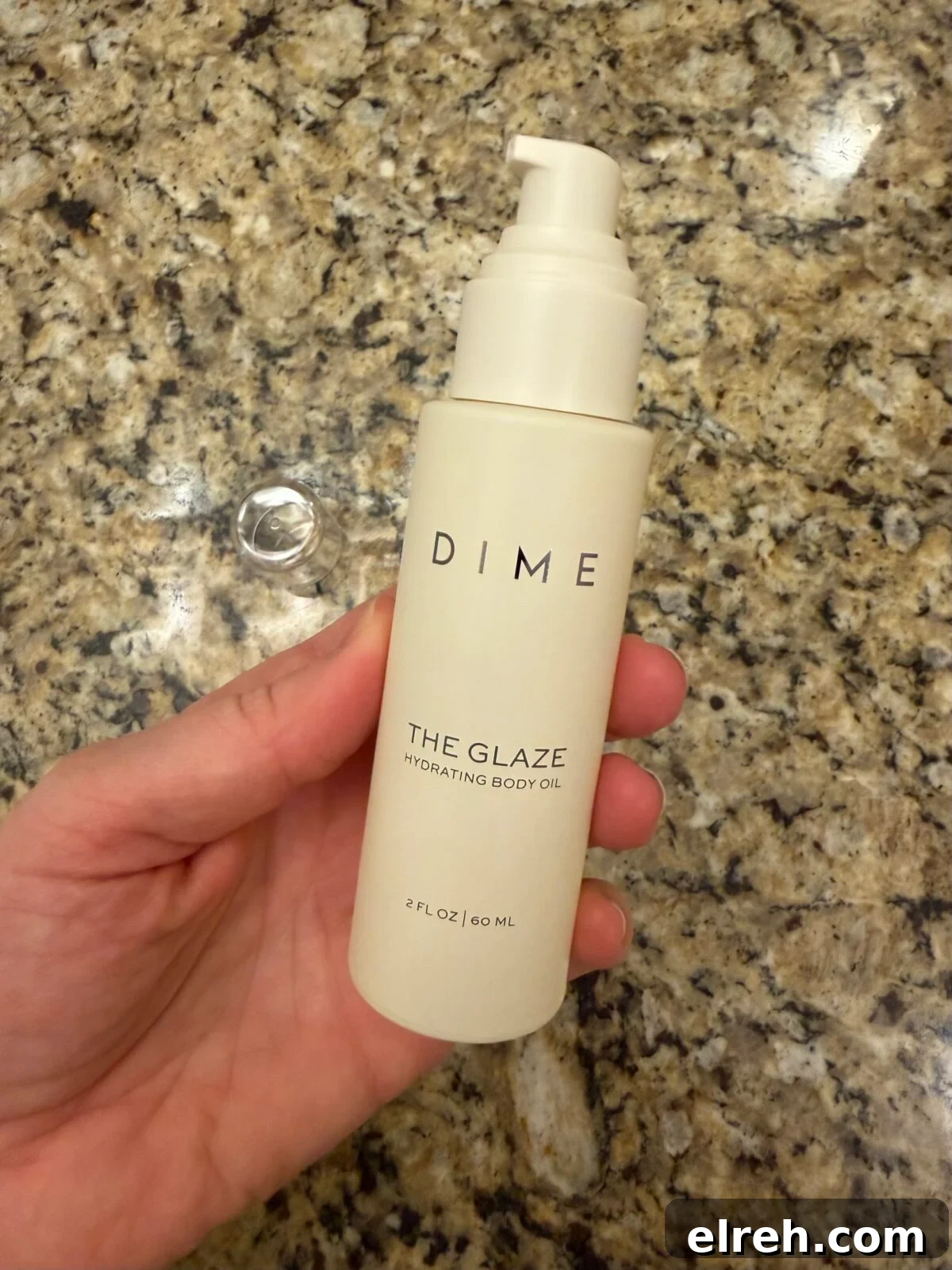 Hand holding DIME The Glaze body oil bottle