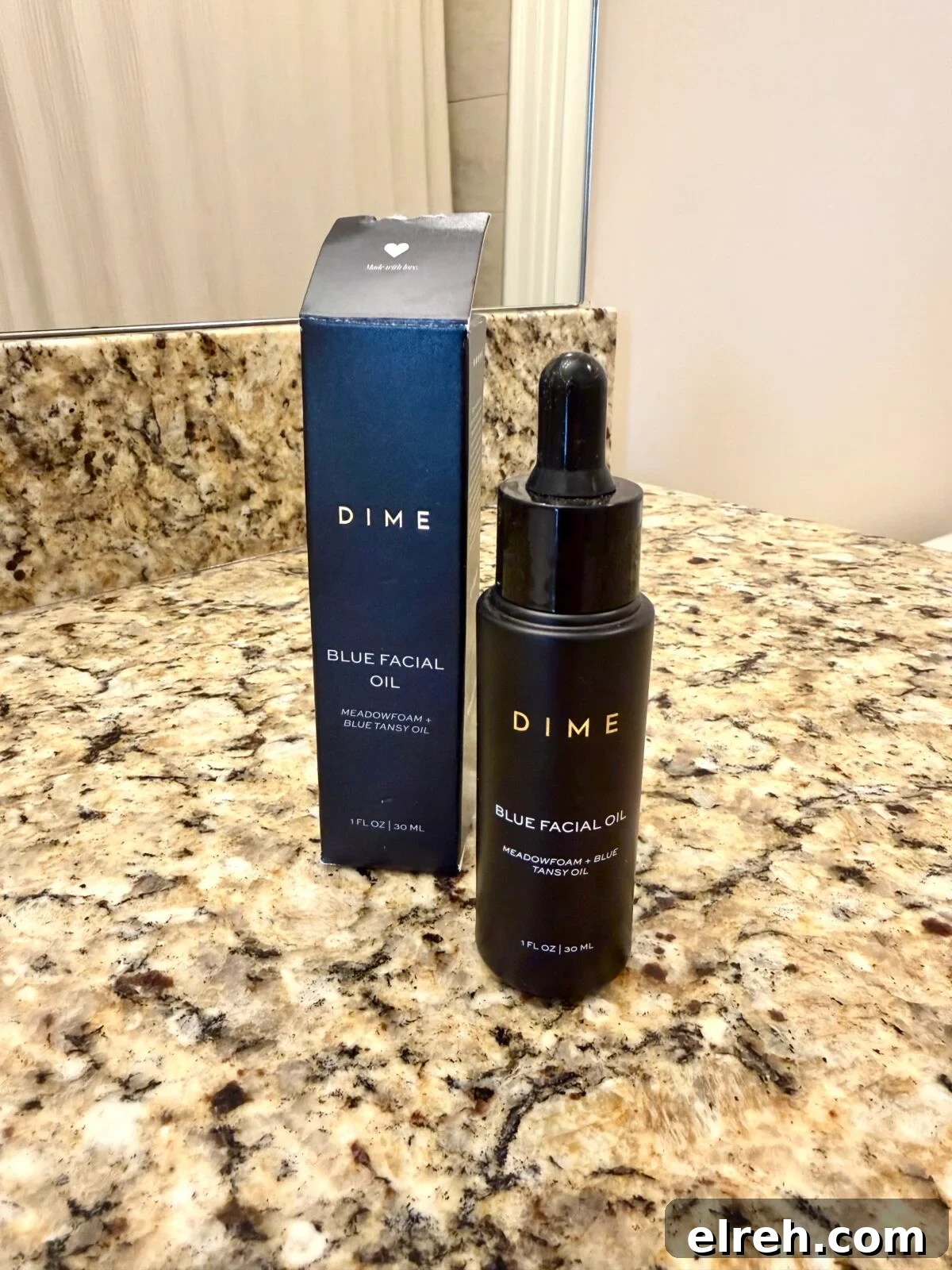 A bottle of DIME Blue Facial Oil with a dropper is placed next to its matching box