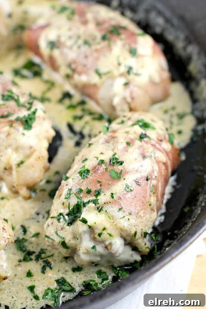 chicken thighs in a cast iron skillet, wrapped in prosciutto, cheese sauce spooned over