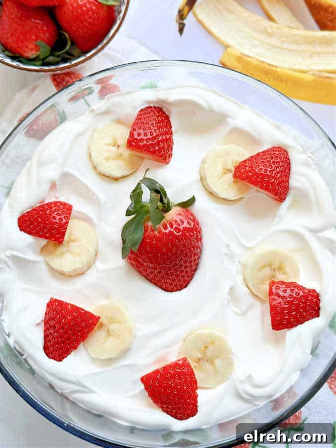 pudding in a clear glass trifle bowl garnished with fresh strawberries and sliced bananas