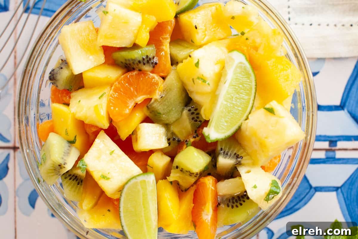 A bowl of Mexican fruit salad on a table with limes and kiwis.