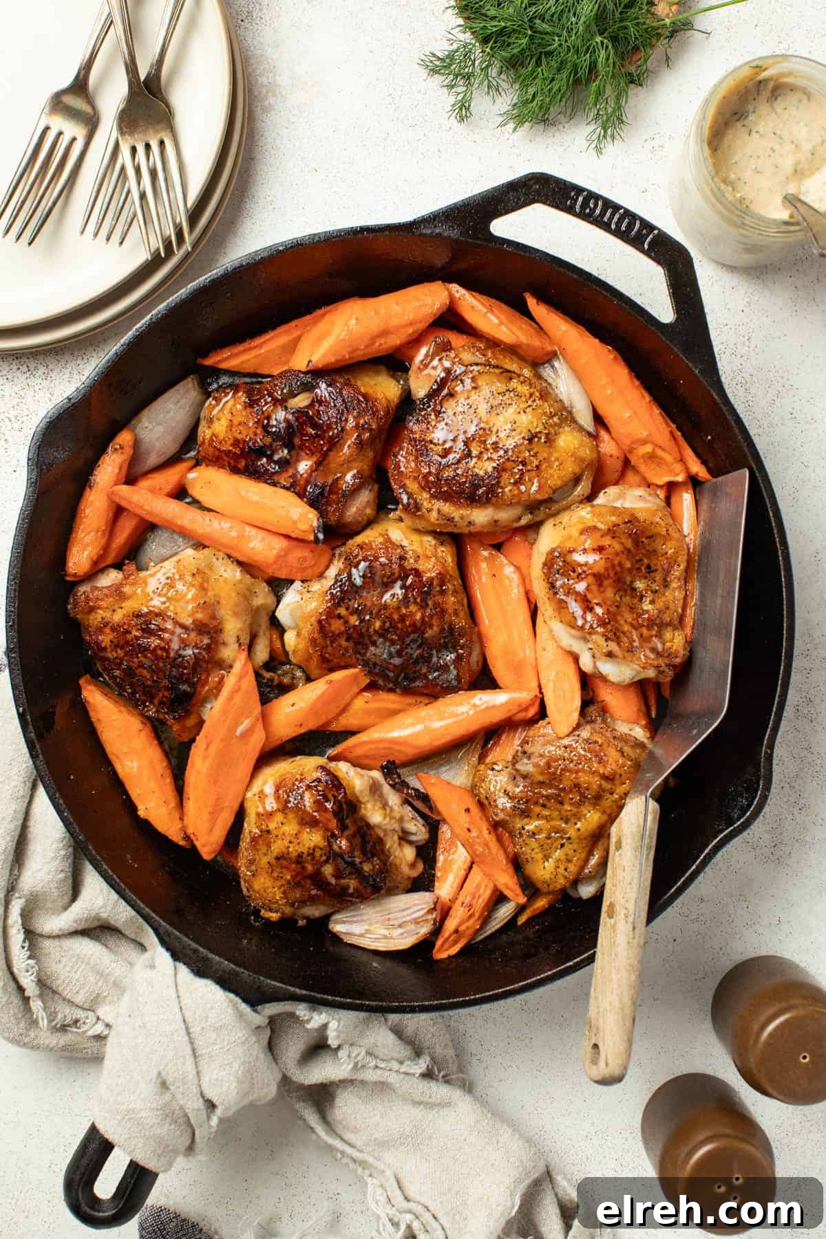 Chicken thighs with carrots and shallots in a black cast iron skillet after being seared till crispy next to fresh dill and a tahini sauce.