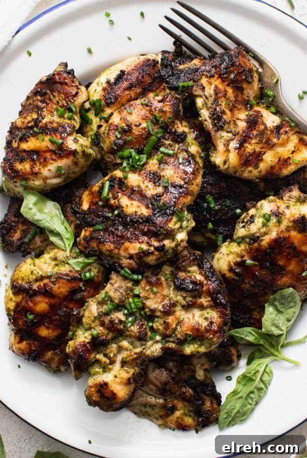 Grilled boneless chicken thighs on a white plate with a fork and basil leaves.