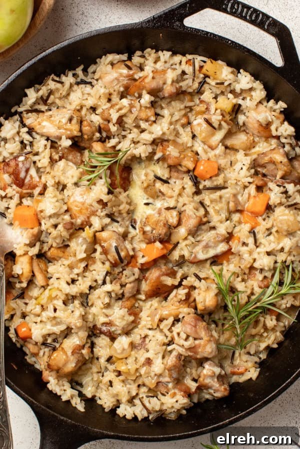 A chicken and wild rice skillet with fresh herbs and vegetables on a white table.
