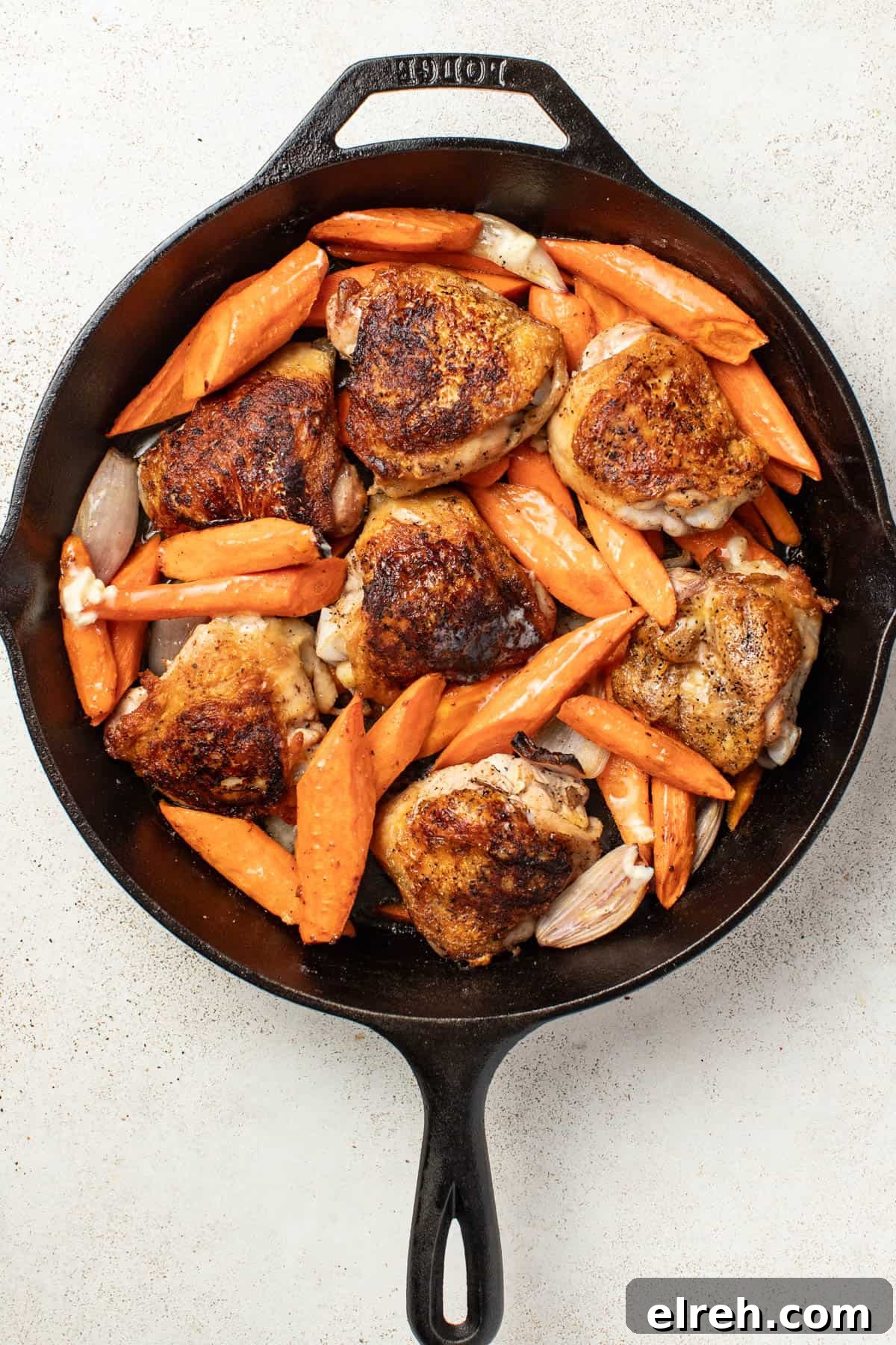 Chicken thighs with carrots and shallots in a cast iron skillet after being seared and finished cooking in the oven.