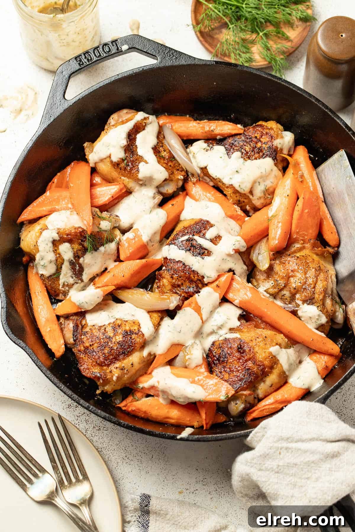 Chicken thighs and carrots in a skillet topped with a tahini sauce.