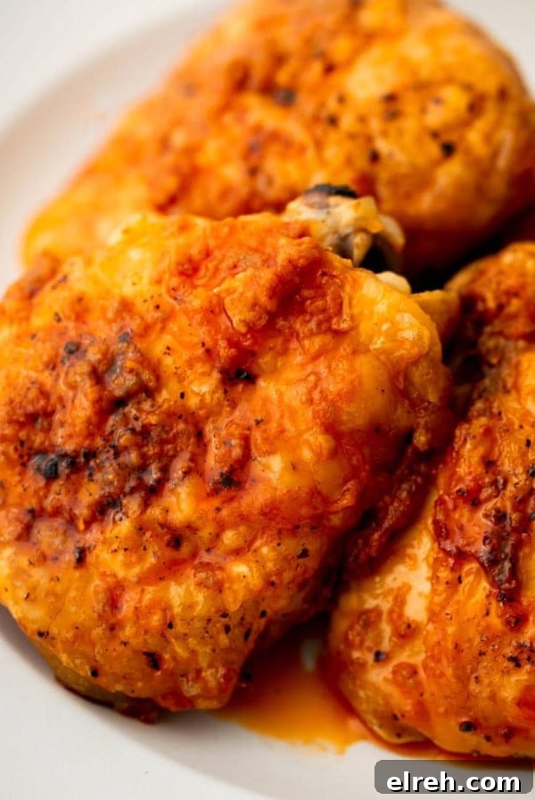 Four buffalo chicken thighs stacked on a white plate.