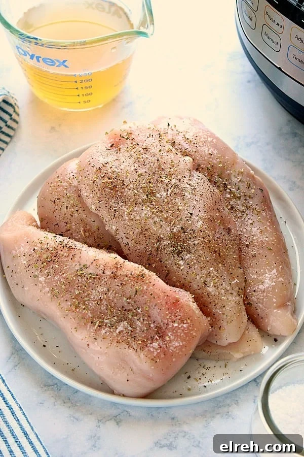 How to make the best shredded chicken in the Instant Pot pressure cooker. Overhead shot of raw chicken breasts, seasoned, on white plate.