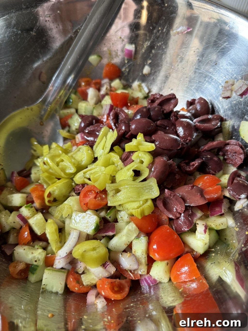 Chopped and marinated tomatoes, olives, cucumbers, peppers, and onions in a metal bowl