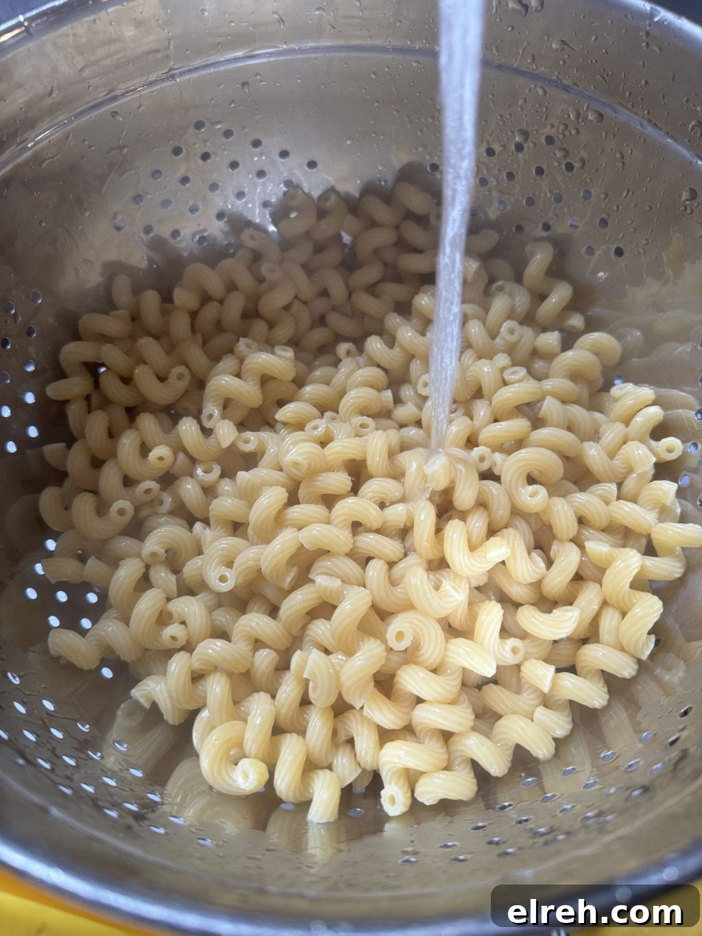 Pasta in a strainer being washed with tap water