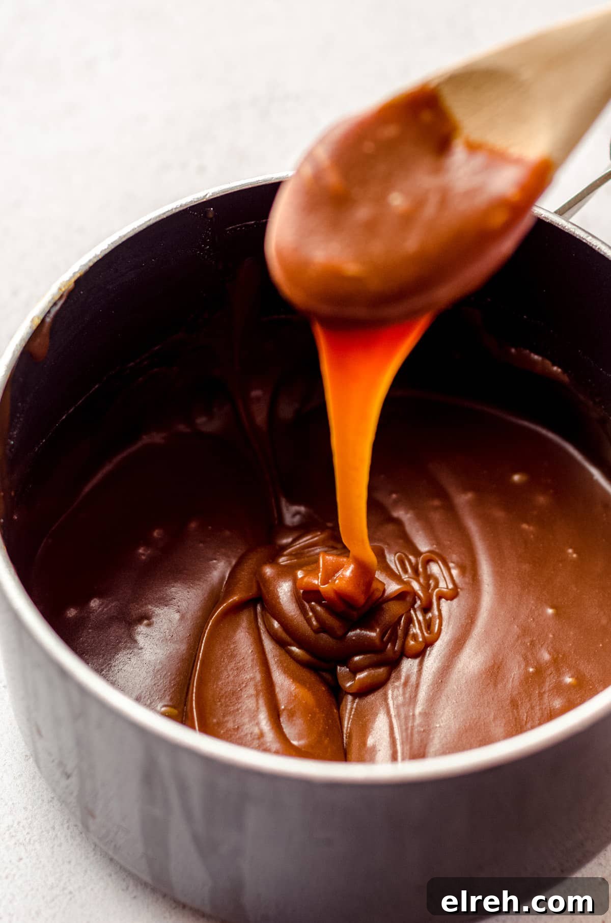 wooden spoon dipped into a saucepan of salted caramel sauce and dripping it back into the pan