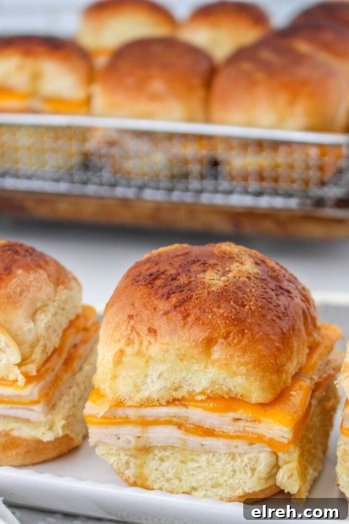 sliders on a tray with more sliders in a baking tray behind it on table 