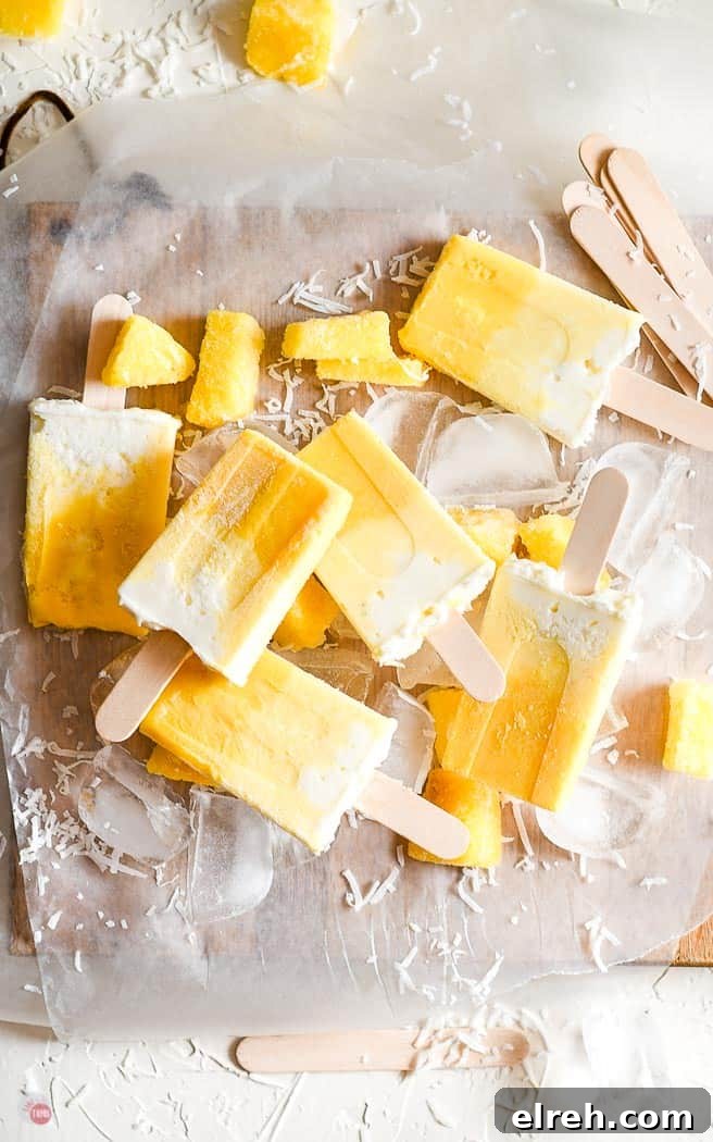 Creamy Mango Pina Colada Popsicles Recipe 2 ombre fruit popsicles on parchment paper with ice cubes