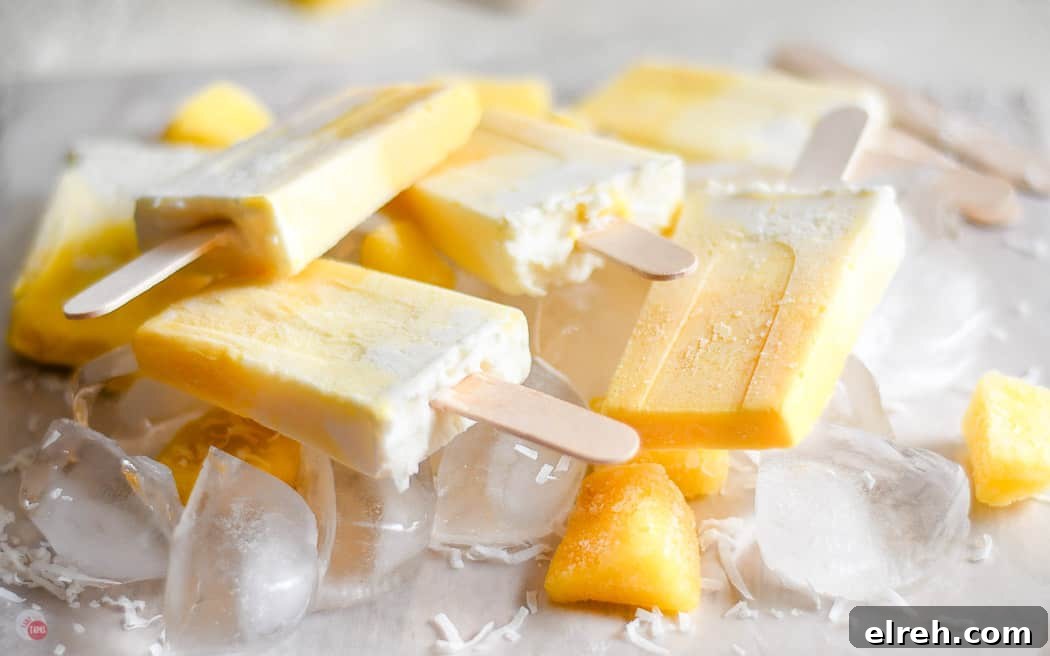 Creamy Mango Pina Colada Popsicles Recipe 3 side view of obmre colored popsicles on a bed of ice cubes