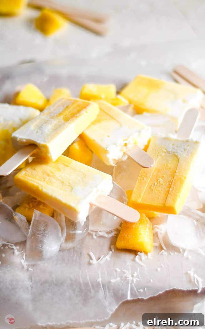 Creamy Mango Pina Colada Popsicles Recipe 9 pile of popsicles on parchment paper topped with ice cubes