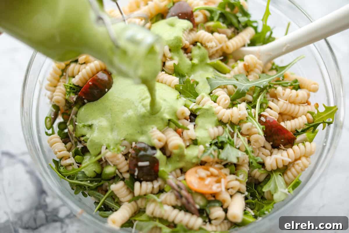 Creamy Green Goddess Pasta Salad with Avocado and Herbs 5 Process shot of someone pouring the dressing over the combined salad ingredients.