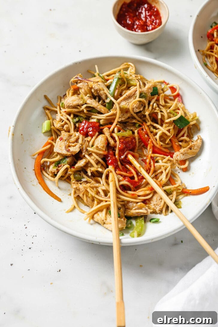 A bowl of Hakka Noodles topped with chili garlic sauce alongside chopsticks.