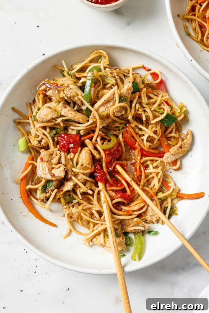 Top view of a bowl of Hakka Noodles topped with chili garlic sauce alongside chopsticks.