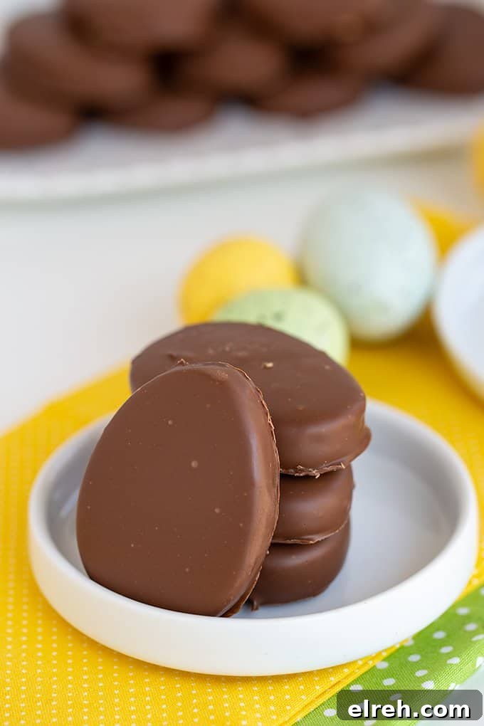 Chocolate Peanut Butter Eggs Recipe 9 peanut butter eggs stacked with a single egg leaned against the stack on a white plate with speckled eggs behind it