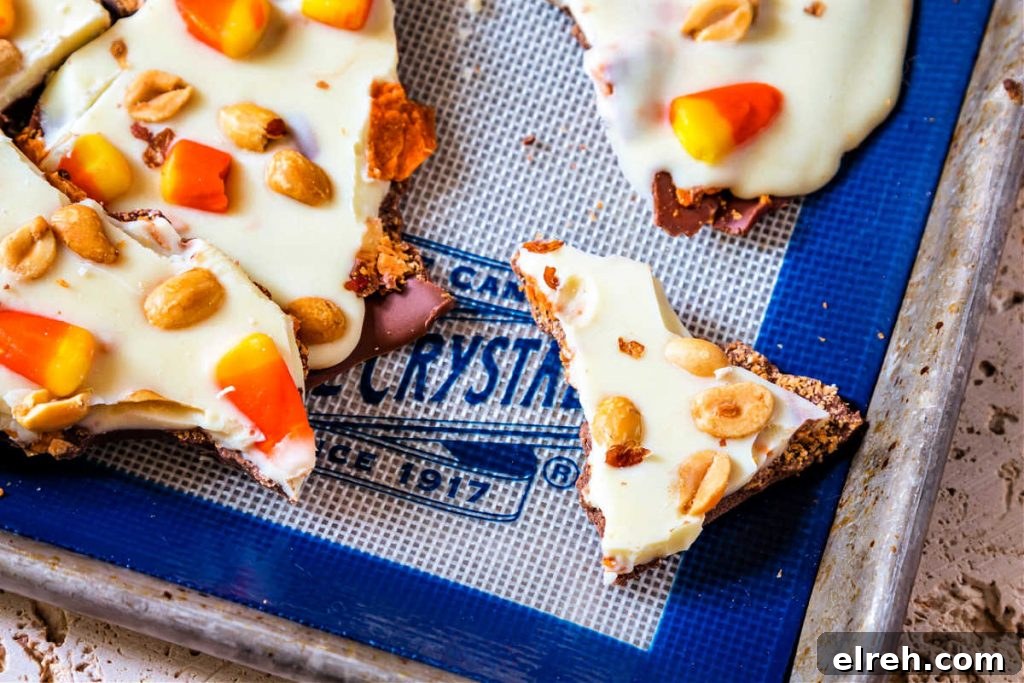 An overhead shot of pieces of candy bark with candy corn and peanuts on a white and blue baking mat.