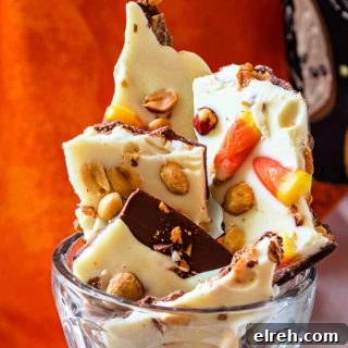 A close up of pieces of milk and white chocolate bark studded with crushed Butterfinger, peanuts, and candy corn.