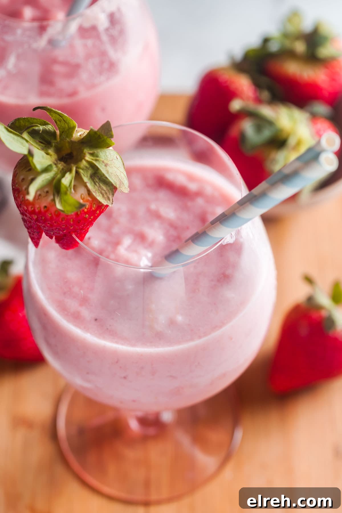 A closeup view of two large glasses filled with strawberry banana smoothies. Garnished with fresh berries and striped straws.