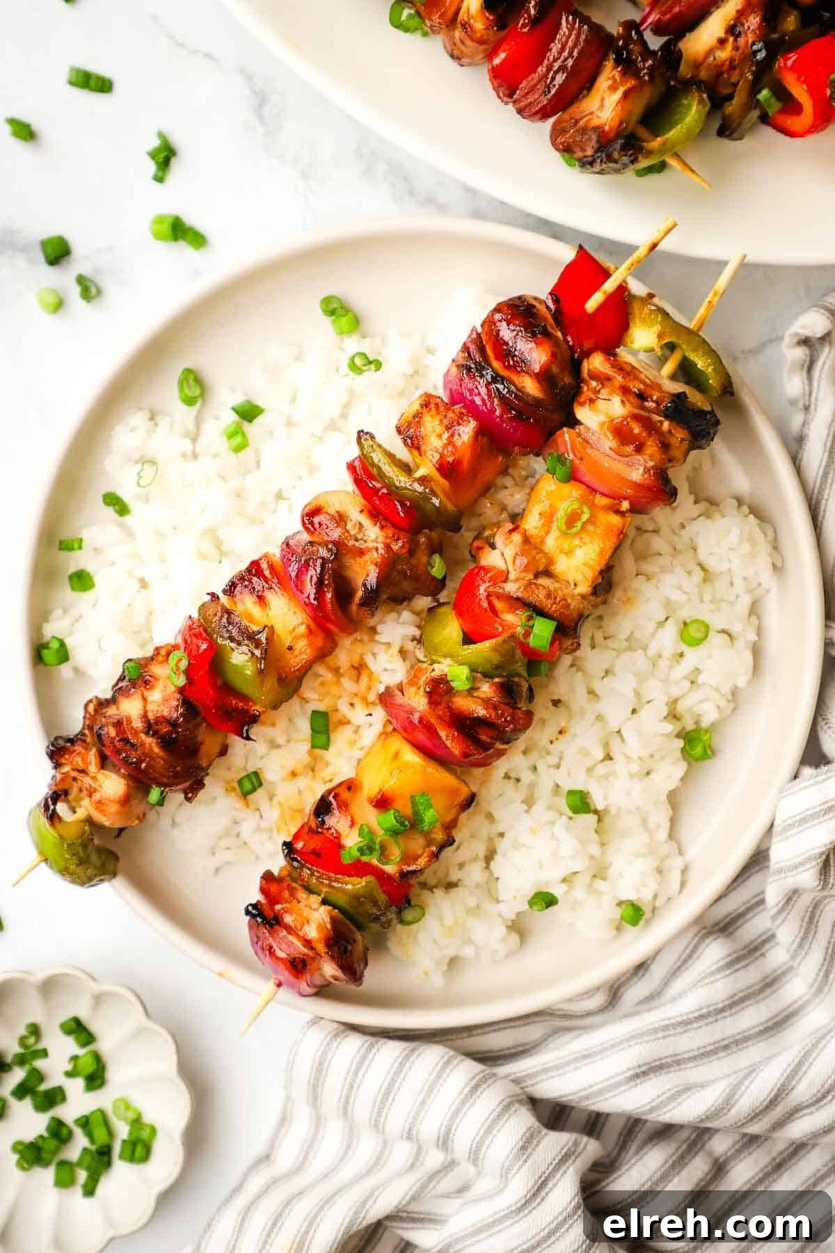 A plate of teriyaki chicken and vegetable skewers served over rice.