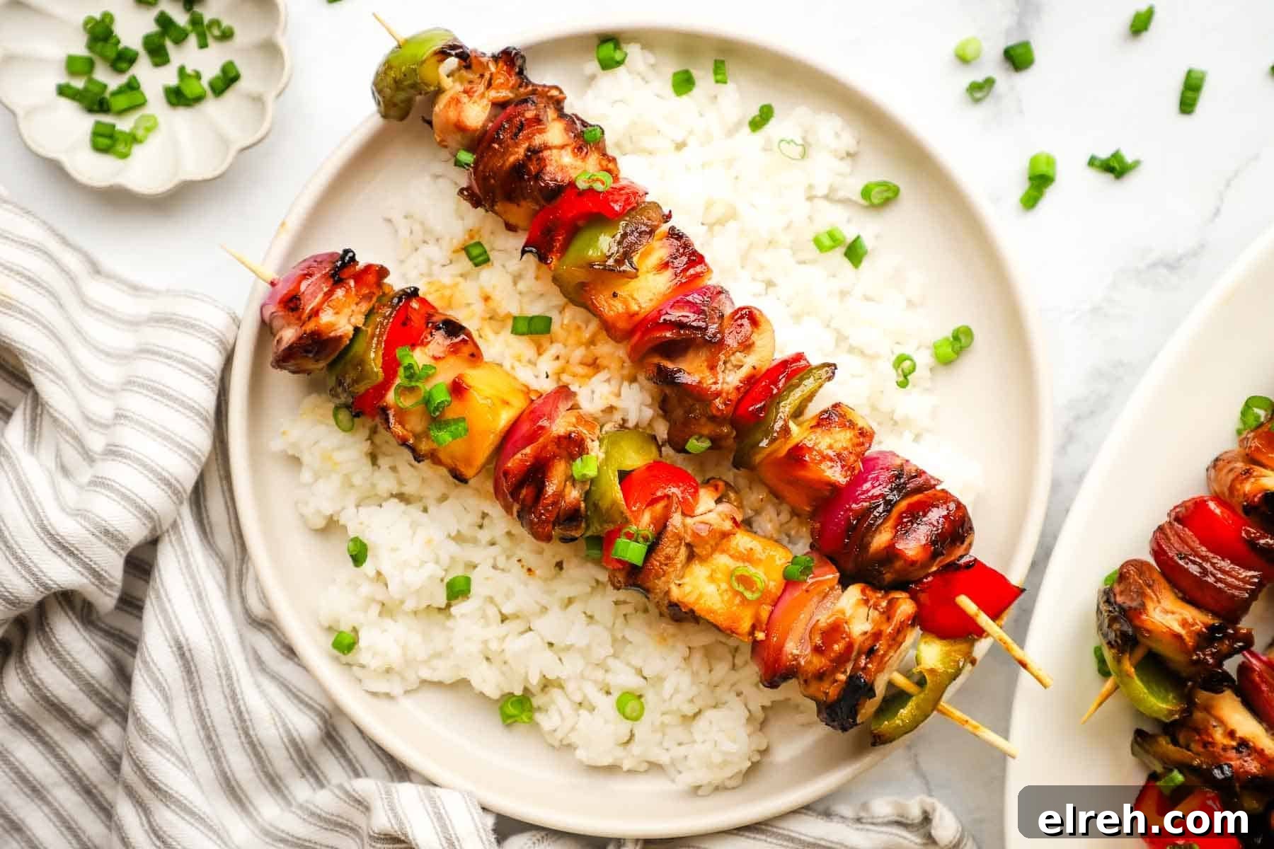 A plate of teriyaki chicken and vegetable skewers served over rice.